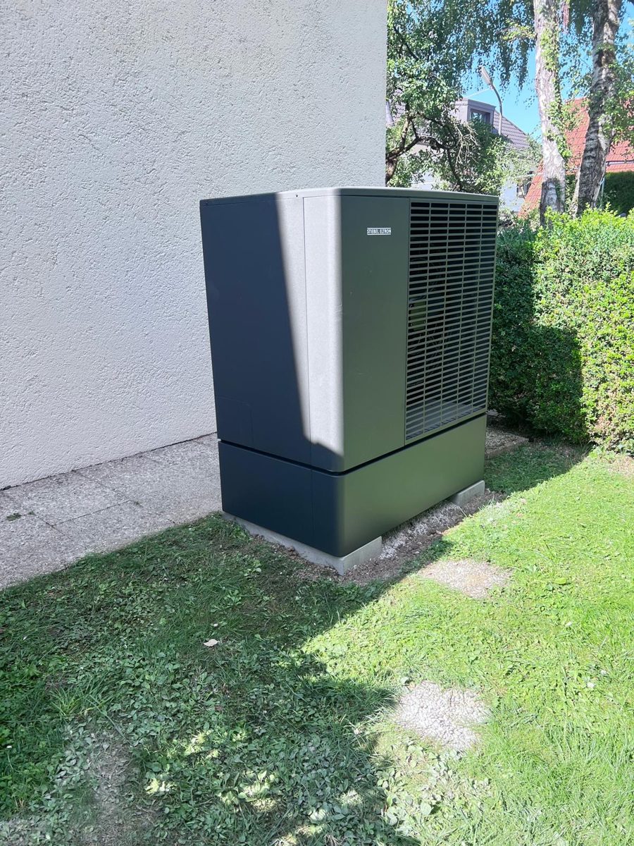 Von Ferdinand Schatz installierte Luft-Wasser-Wärmepumpe an einer Hausecke mit Hecke